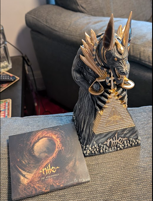 A photo of the CD copy of Nile's "The Underworld Awaits Us All" album, next to a statue of Anubis with the Nile logo